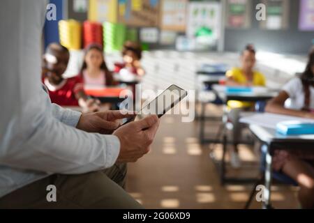 Mid section of male teacher using digital tablet while sitting in the class at elementary school Stock Photo