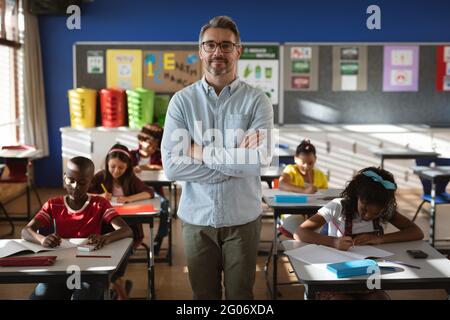 Portrait of caucasian male teacher with arms crossed standing in class at elementary school Stock Photo