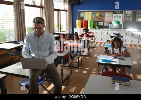 Caucasian male teacher using laptop while sitting in the class at elementary school Stock Photo