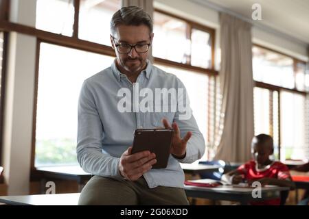 Caucasian male teacher using digital tablet while sitting in the class at elementary school Stock Photo