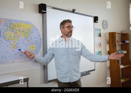 Caucasian male teacher teaching geography to students in the class at elementary school Stock Photo