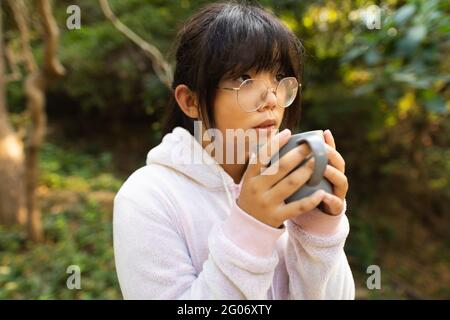 Portrait of asian girl in pink hoodie holding tea mug standing in garden Stock Photo