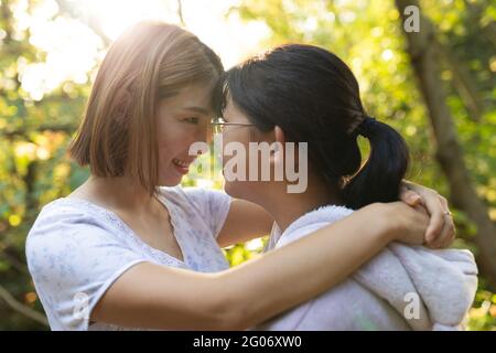 Portrait of smiling asian woman with her daughter touching heads and embracing in garden Stock Photo