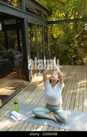 Asian woman practicing yoga with eyes closed on terrace in garden Stock Photo
