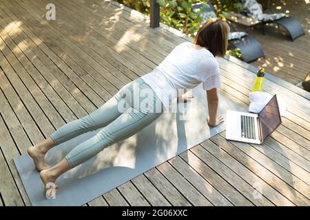 Asian woman practicing yoga using laptop on terrace in garden Stock Photo
