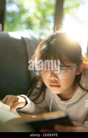 Asian girl in glasses reading a book and lying on sofa Stock Photo