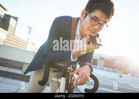 Midsection of asian businessman talking on smartphone leaning on bike in city street Stock Photo