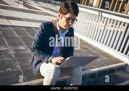 Asian businessman using laptop sitting on steps in city street Stock Photo