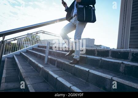 Midsection of businessman using smartphone walking down steps in city street Stock Photo