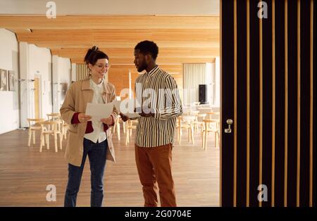 Two business colleagues talking to each other and discussing documents while standing at office Stock Photo