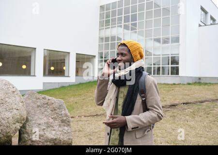 African young man talking on mobile phone while walking in the city in cold weather Stock Photo