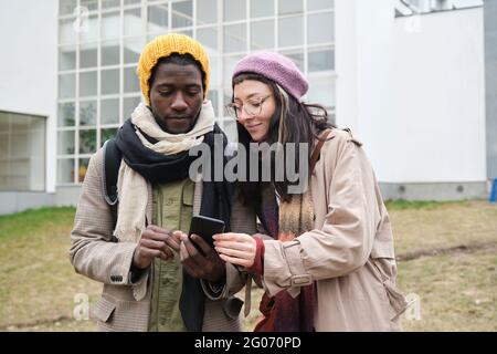 Young couple in warm clothing using mobile phone together outdoors Stock Photo
