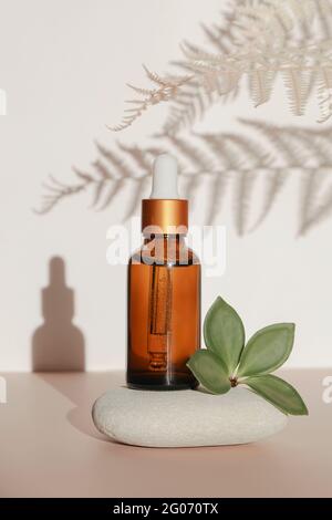 dark amber glass bottle with oil on natural stone with leaf on white background. copy space. natural cosmetics and body care concept , mock up Stock Photo