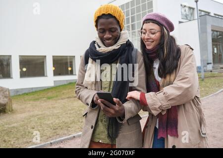 Happy young couple watching photos on mobile phone and laughing while walking outdoors Stock Photo