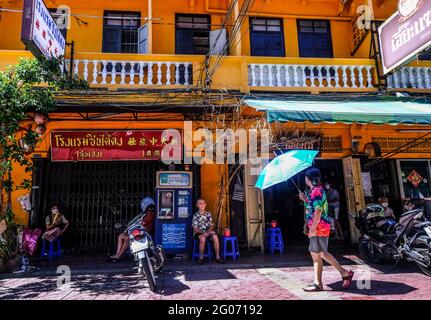 A woman holding an umbrella walks past a group of people in Chinatown, Bangkok, Thailand Stock Photo