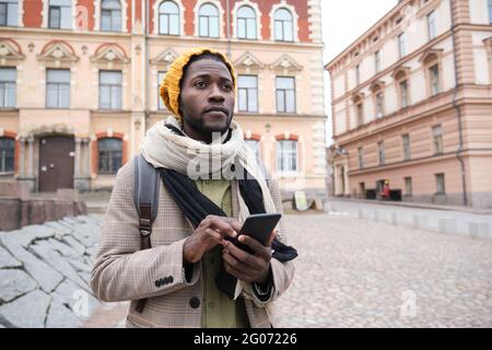 African man in warm clothing using mobile phone while standing in the city Stock Photo