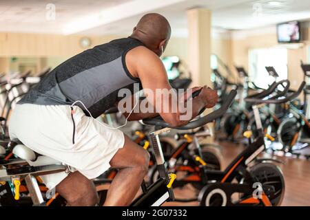 View of unrecognizable black person doing exercise bike in fitness center. Healthy lifestyle concept. Stock Photo