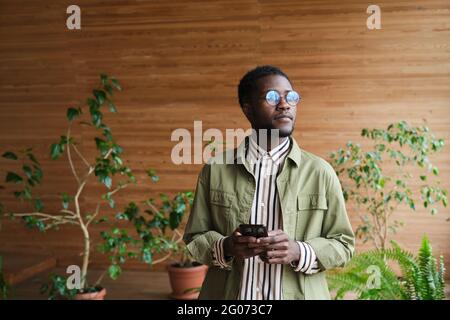 African young man in eyeglasses using mobile phone while standing in modern hall Stock Photo