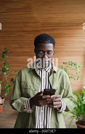 African young businessman typing a message on mobile phone while standing at office Stock Photo