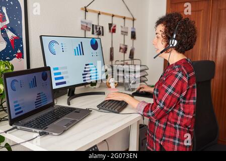 Woman teleworking at adjustable desk standing and talking on headset Stock Photo