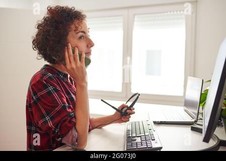Woman teleworking at an adjustable standing desk and talking on the phone Stock Photo