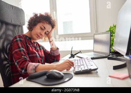 Woman tired of working in front of the computer rests her head on her hand Stock Photo