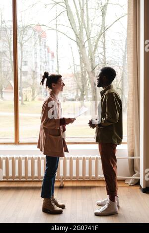 Young people discussing report together while standing against the big window Stock Photo
