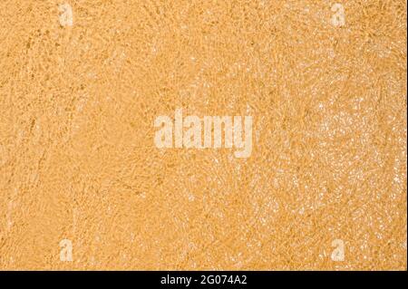 sand and water texture. clear sea water waves on top of golden sand on the beach. Texture of wet sand on a beach, for summer background Stock Photo