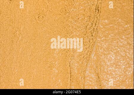 Close-up of wave on sandy beach with copy space for your text, top view background. transparent water texture. golden sand is visible through the clea Stock Photo