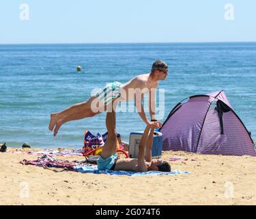 Bournemouth, Dorset, UK, 1st June 2021, UK Weather: First day of meteorological summer set to be the hottest day of the year so far. A young man performs acrobatics with a friend on the beach and enjoying the early summer heatwave in which temperatures are in the mid-twenties across much of England. Credit: Paul Biggins/Alamy Live News Stock Photo