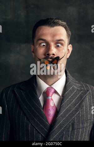 Close- up portrait of young man with butterfly looking at camera isolated on grey vintage background. Stock Photo