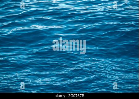 Blue water surface with bright sun light reflections, water in ocean or sea background closeup. Blue sea texture with waves and foam. Blue sea water s Stock Photo