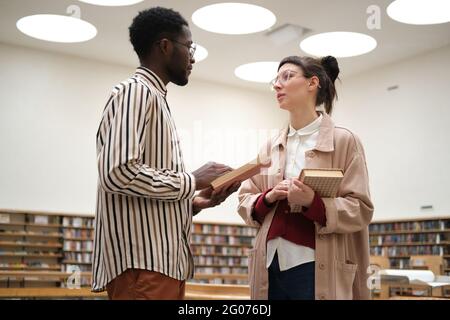 Two students discussing books and studying while standing in the library Stock Photo