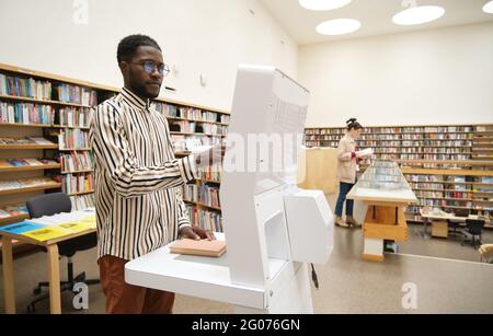 African young man standing in the library and choosing books for reading Stock Photo