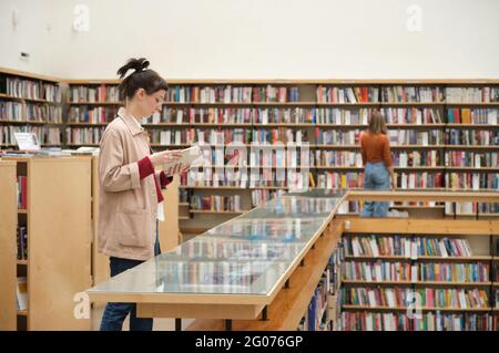 Young people studying in the library and choosing books for reading Stock Photo
