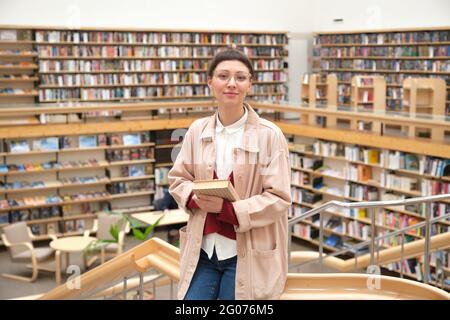 Portrait of young woman with book standing in the big library Stock Photo