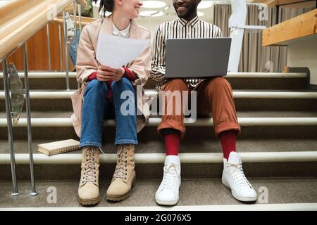 Young couple with laptop and documents sitting on stairs and studying in team Stock Photo
