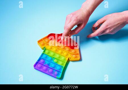 Girl reaches out with her hands to colorful trendy pop it toy in form t-shirt on blue background. Stock Photo