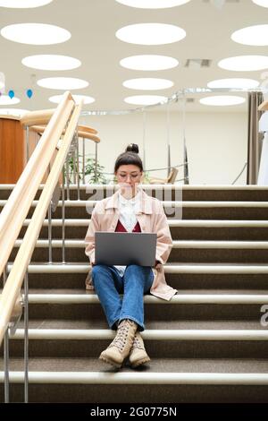 Young woman sitting on stairs and using laptop for study Stock Photo
