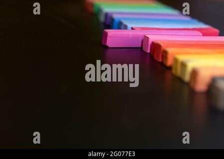 Colorful chalks on a blackboard. One of the chalks sticks out from the others. Empty black background for text. Concept of standing out, back to schoo Stock Photo