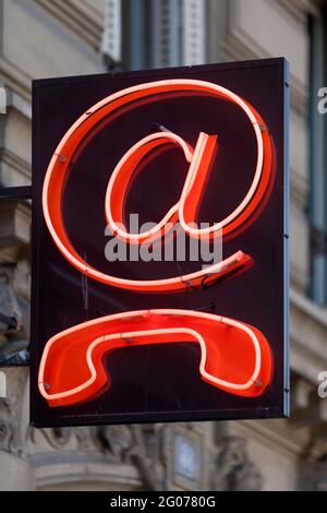 Outdoors red neon sign shaped into an @ and a phone. Stock Photo