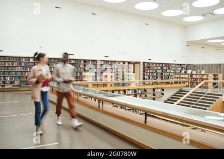Blurred motion of people walking along the corridor in big library Stock Photo
