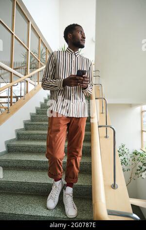 African young man using mobile phone while standing on stairs at office building Stock Photo