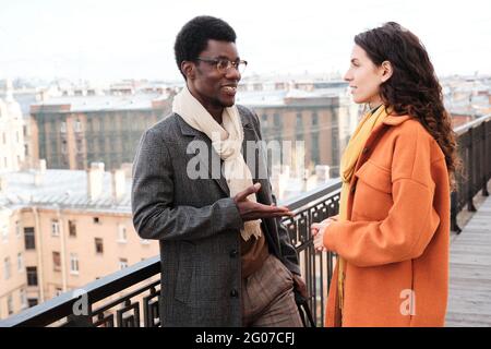 Man and woman talking to each other while standing on balcony outdoors Stock Photo