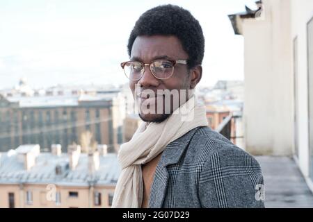 Portrait of African young man in eyeglasses and in warm clothing standing on the balcony Stock Photo