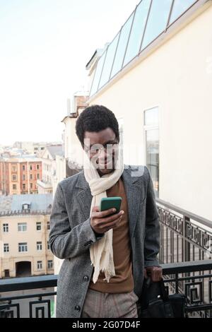 African man in eyeglasses using mobile phone while standing on balcony outdoors Stock Photo