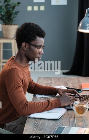 African young man sitting at the table and using computer for his study at home Stock Photo