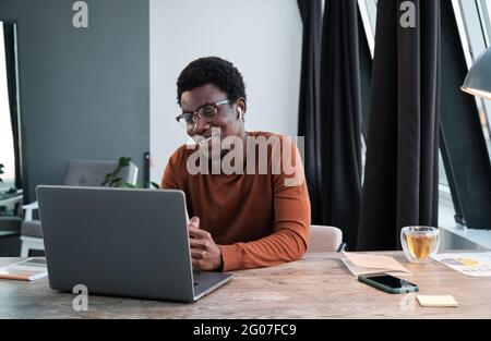 African businessman sitting at the table talking online and smiling he using laptop Stock Photo
