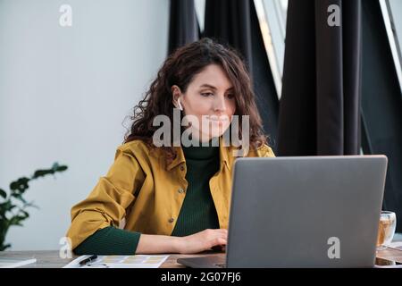 Young businesswoman in headphones watching something on laptop while sitting at her workpalce Stock Photo