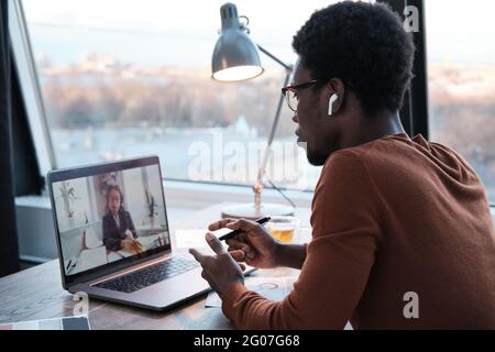 African young businessman talking to his colleague online using laptop while working at office Stock Photo